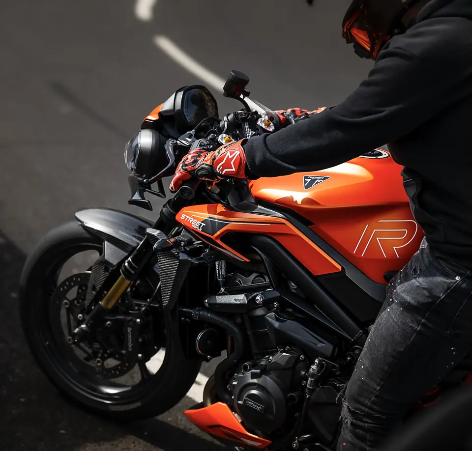 Detalle de una moto naranja y su piloto en la carretera