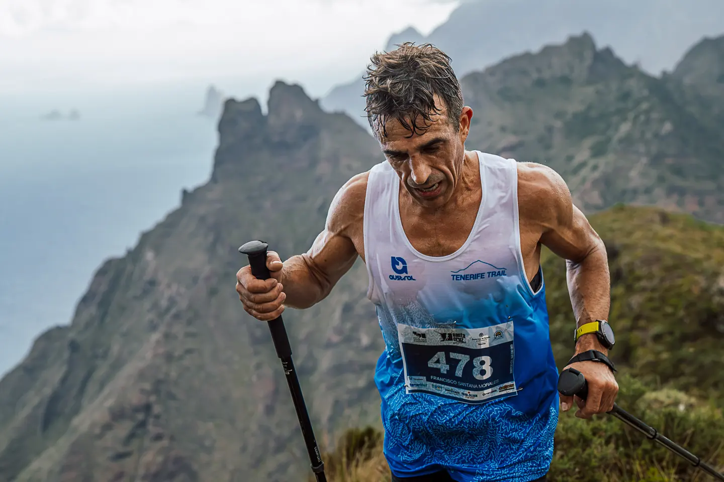Corredor de trail con bastones y dorsal 478 frente a los riscos