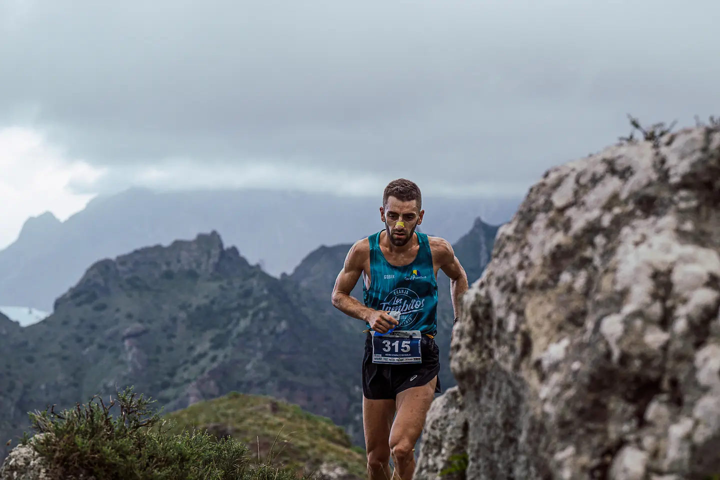 Corredor de trail entre rocas y montañas al fondo